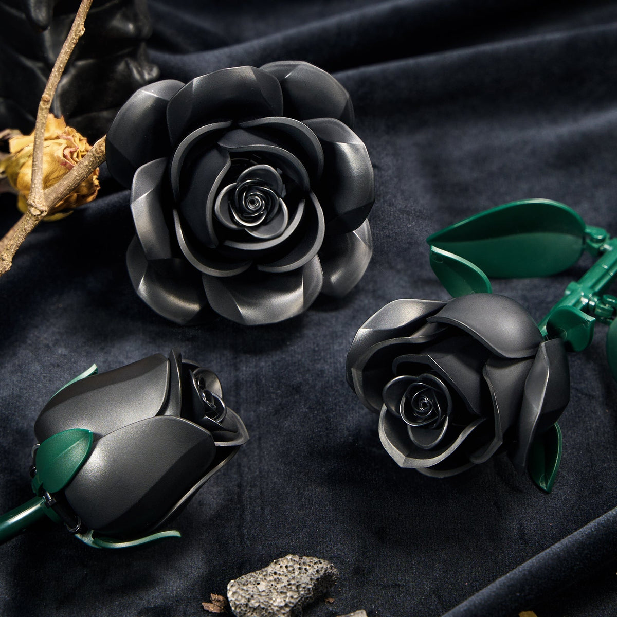 Black rose building blocks on dark velvet - matte petals and green leaves in close-up