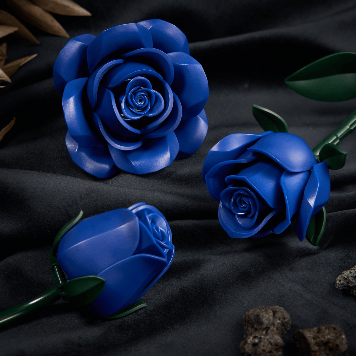 Blue rose building blocks on dark velvet - glossy petals and green leaves close-up