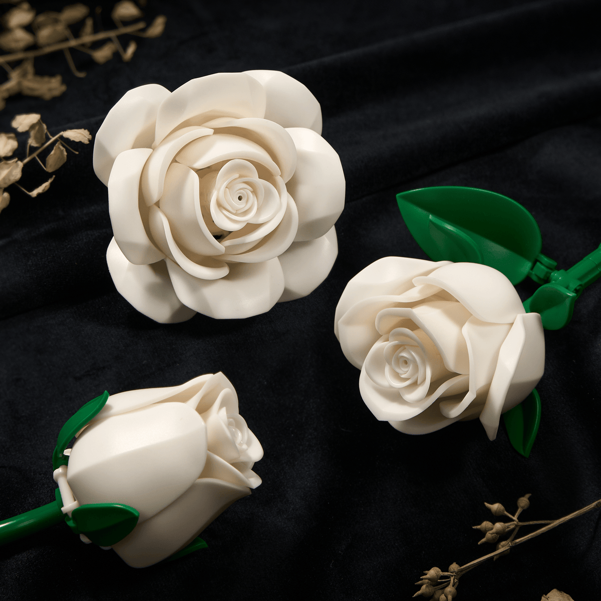 Two white roses on black velvet - one open bloom and one bud, with glossy green leaves