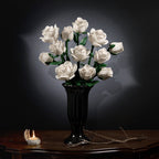 White rose bouquet in a carved black vase on an antique table against a dark background